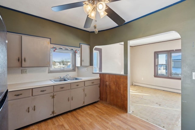 kitchen featuring a sink, light countertops, light wood-type flooring, a ceiling fan, and a baseboard radiator