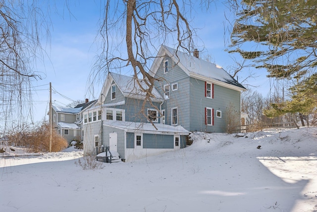 snow covered back of property with a garage and a chimney