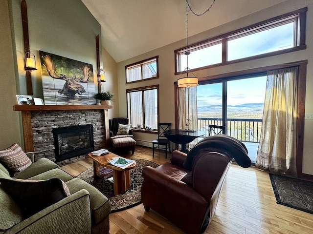 living room with a stone fireplace, light wood-type flooring, and high vaulted ceiling