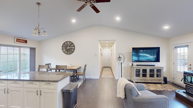 living room with ceiling fan with notable chandelier, dark hardwood / wood-style flooring, and vaulted ceiling