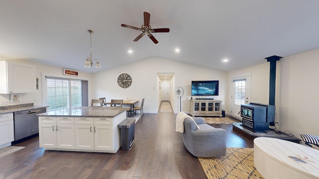 kitchen with a wood stove, white cabinets, hanging light fixtures, stainless steel dishwasher, and light stone counters