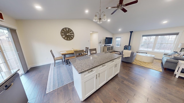 kitchen with a wood stove, white cabinetry, light stone countertops, lofted ceiling, and a kitchen island