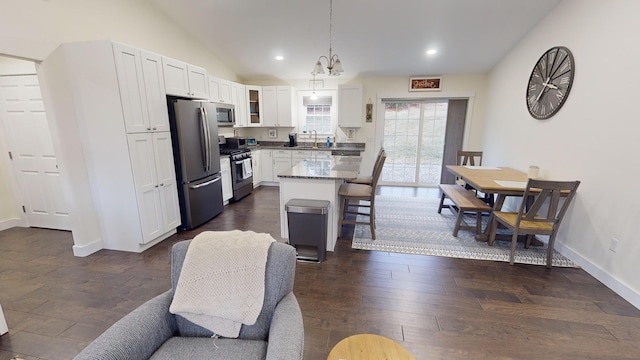 kitchen featuring appliances with stainless steel finishes, dark stone counters, sink, a center island, and hanging light fixtures