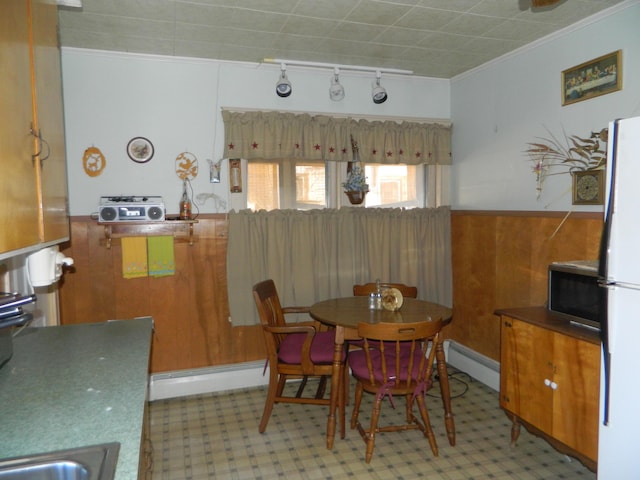 dining space featuring sink, crown molding, wooden walls, and a baseboard radiator