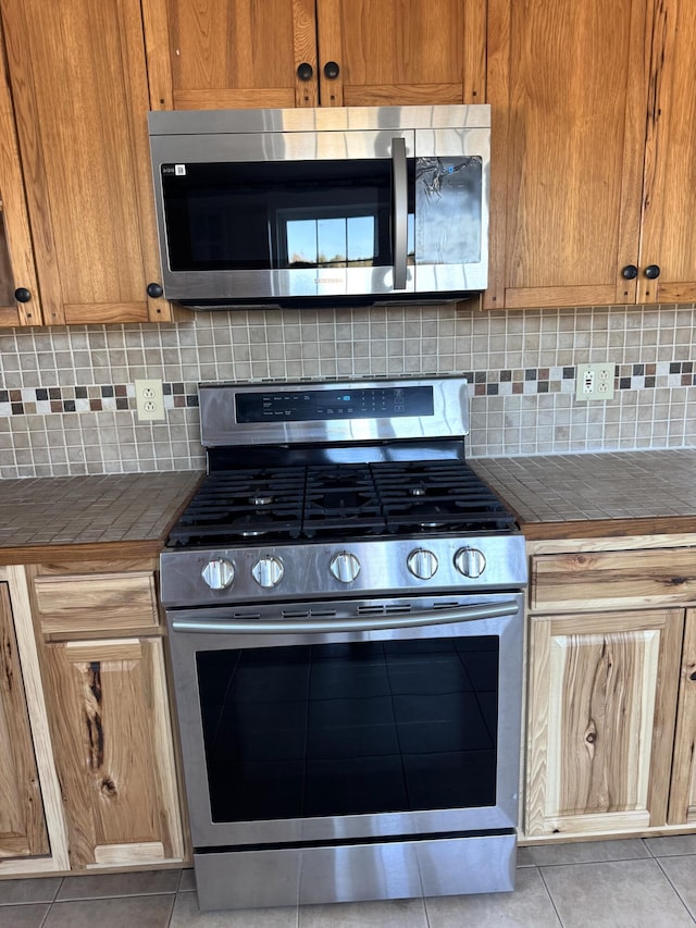 kitchen featuring stainless steel appliances, tile counters, backsplash, and light tile patterned floors