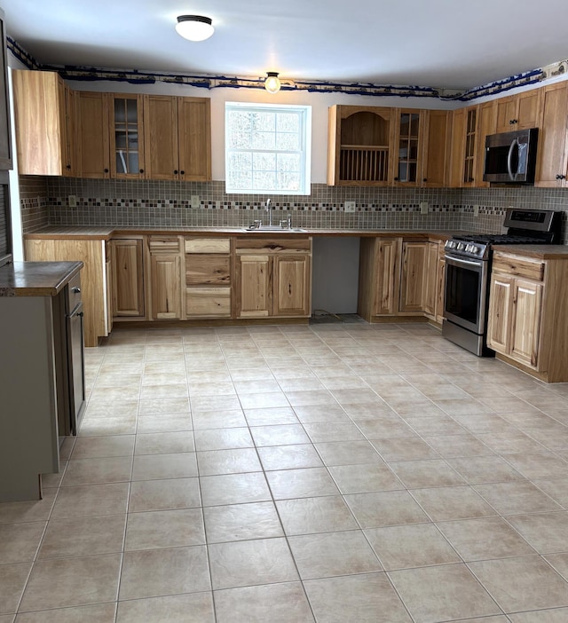 kitchen with stainless steel appliances, glass insert cabinets, backsplash, and light tile patterned floors