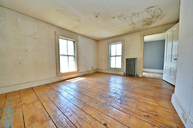 empty room with a wealth of natural light, light wood-type flooring, and radiator