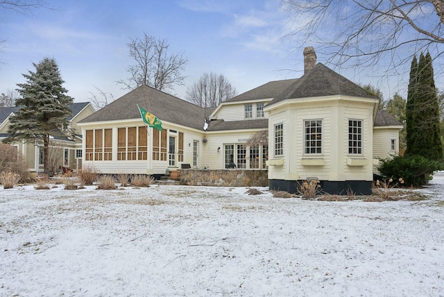 snow covered back of property with a sunroom