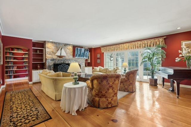 living room with built in features, a stone fireplace, and light wood-type flooring