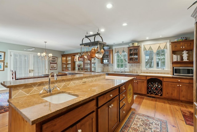 kitchen with a notable chandelier, a center island with sink, sink, hanging light fixtures, and light stone counters