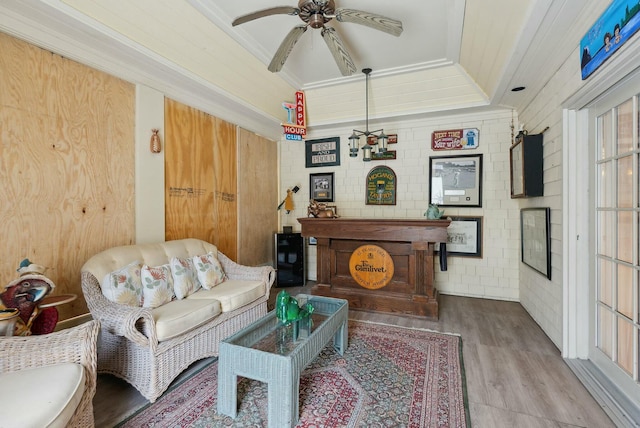 living room with ceiling fan, wood-type flooring, brick wall, and ornamental molding