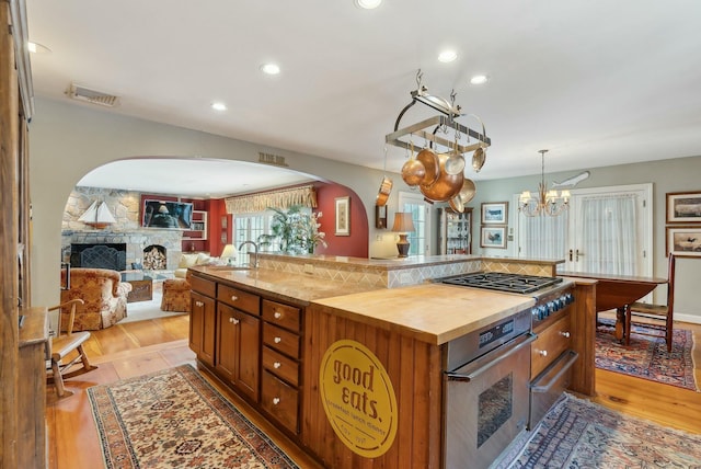 kitchen featuring wood counters, a stone fireplace, an island with sink, appliances with stainless steel finishes, and a notable chandelier