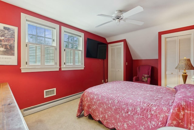 carpeted bedroom with ceiling fan, a baseboard heating unit, lofted ceiling, and multiple closets