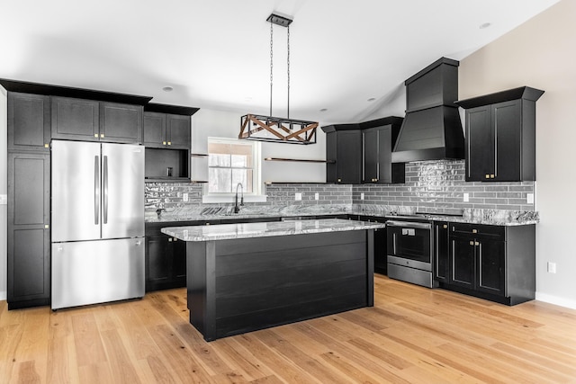 kitchen featuring light wood-type flooring, decorative light fixtures, a kitchen island, custom range hood, and stainless steel appliances