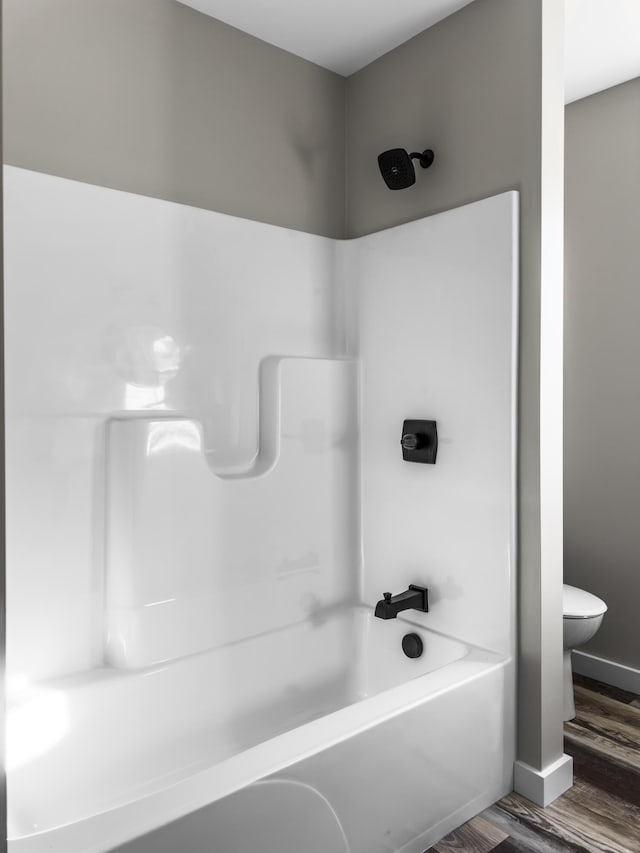 bathroom featuring hardwood / wood-style flooring, toilet, and washtub / shower combination