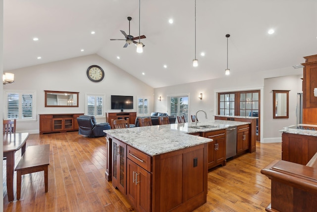 kitchen featuring a large island with sink, sink, hanging light fixtures, appliances with stainless steel finishes, and light stone counters