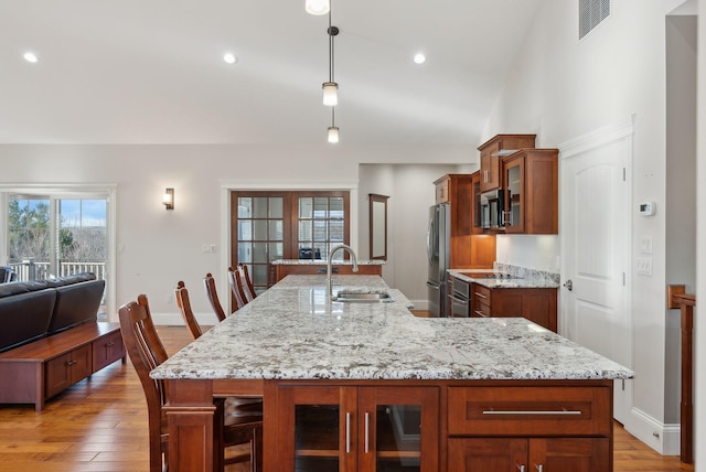 kitchen with sink, stainless steel appliances, an island with sink, decorative light fixtures, and a breakfast bar