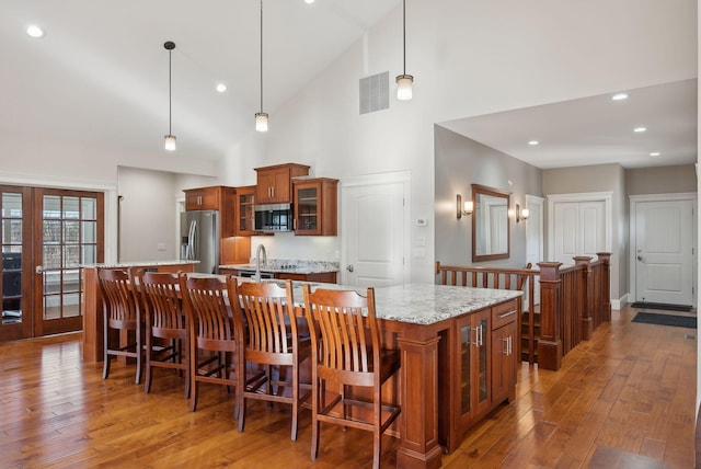 kitchen with a large island, high vaulted ceiling, pendant lighting, a kitchen bar, and appliances with stainless steel finishes