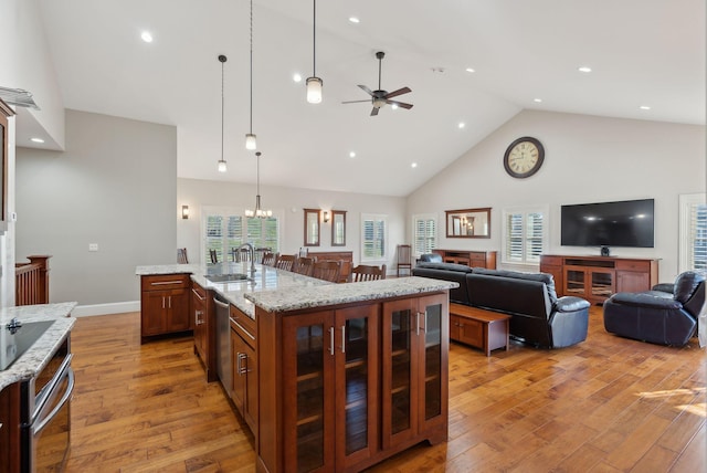 kitchen with sink, light hardwood / wood-style flooring, ceiling fan, an island with sink, and light stone counters