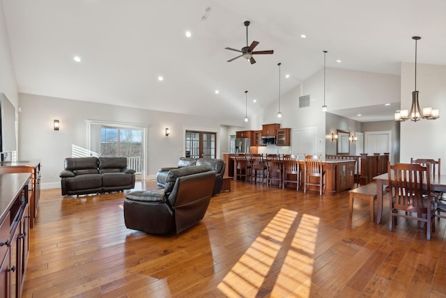 living room featuring ceiling fan with notable chandelier, high vaulted ceiling, and dark wood-type flooring