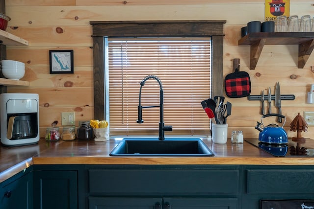 kitchen with blue cabinetry, butcher block counters, wooden walls, and sink