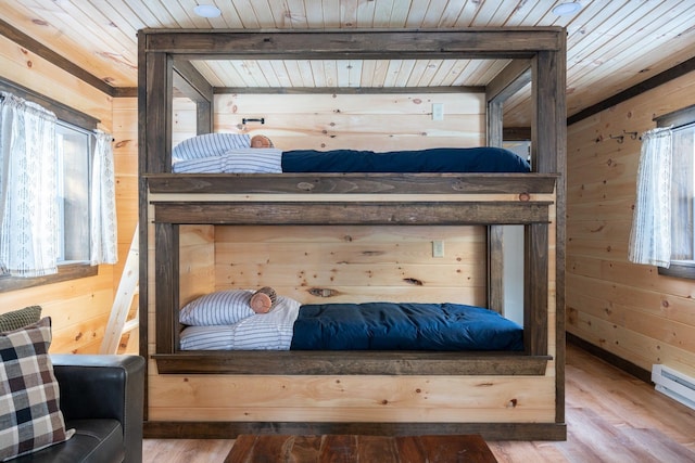 bedroom featuring baseboard heating, wood walls, wooden ceiling, and hardwood / wood-style flooring