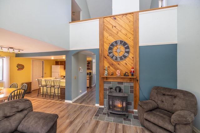 living room with hardwood / wood-style floors, a wood stove, and a towering ceiling