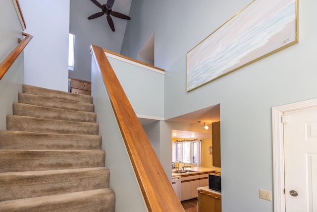 staircase with ceiling fan, sink, and a high ceiling