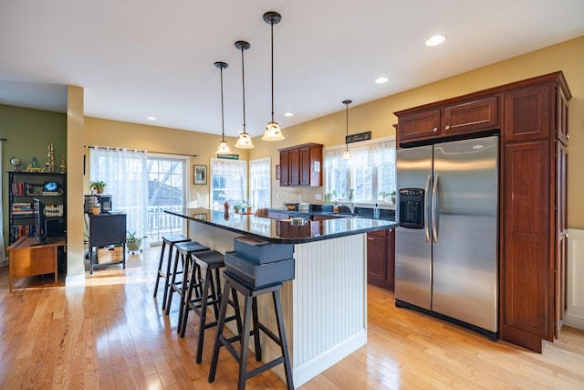 kitchen featuring stainless steel refrigerator with ice dispenser, decorative light fixtures, a center island, and light hardwood / wood-style floors