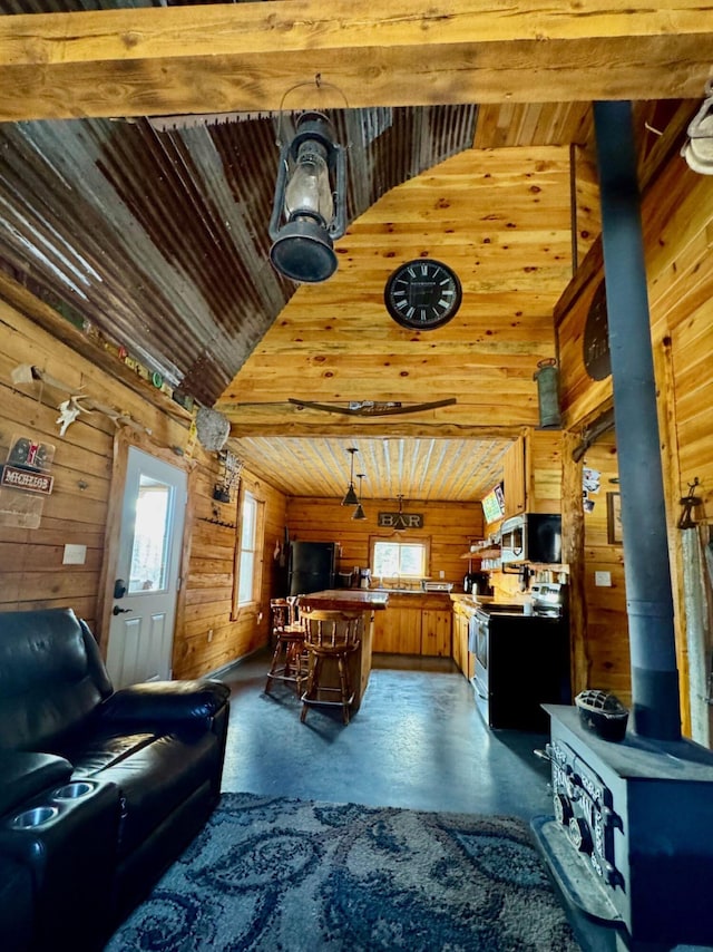 154 Old Brownville Rd, Sebec, ME 04481 - living area featuring high vaulted ceiling, wood walls, a wood stove, wooden ceiling, and concrete floors