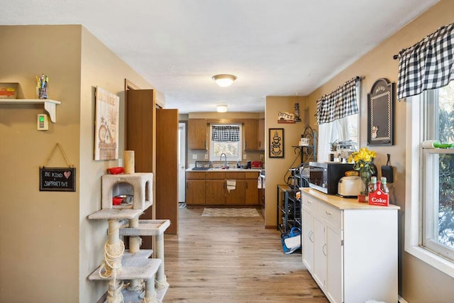 kitchen with white cabinets, brown cabinets, light countertops, light wood-type flooring, and a sink