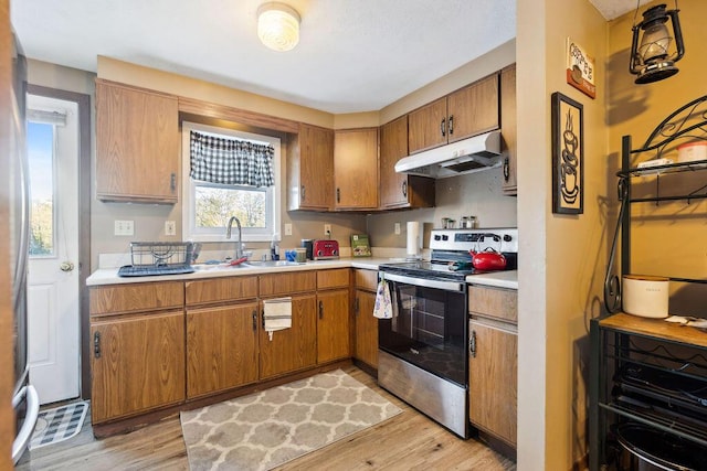 kitchen featuring light wood-style flooring, under cabinet range hood, a sink, light countertops, and stainless steel electric stove