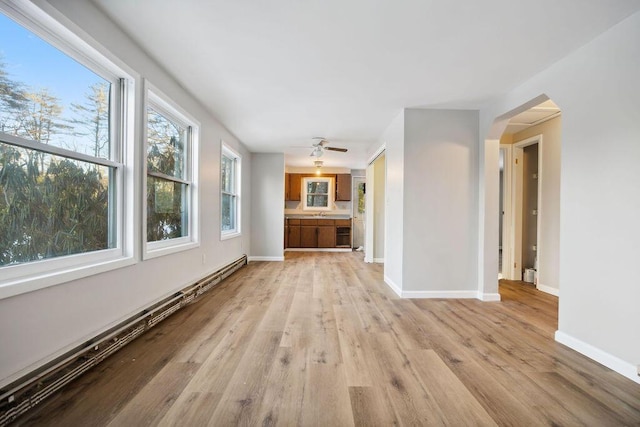 unfurnished living room with light wood-style flooring, baseboards, baseboard heating, and a ceiling fan