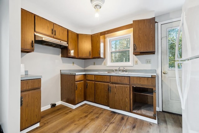 kitchen featuring under cabinet range hood, wood finished floors, baseboards, light countertops, and brown cabinetry