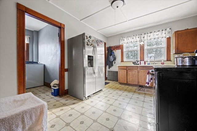 kitchen featuring sink, range with electric cooktop, washer / clothes dryer, radiator heating unit, and stainless steel refrigerator with ice dispenser