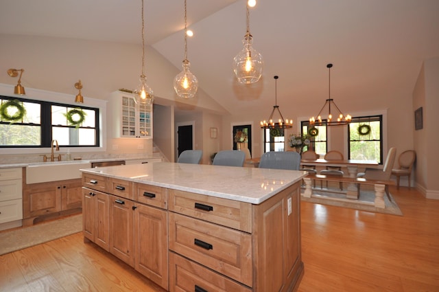 kitchen featuring light stone countertops, light wood-type flooring, sink, a notable chandelier, and a center island