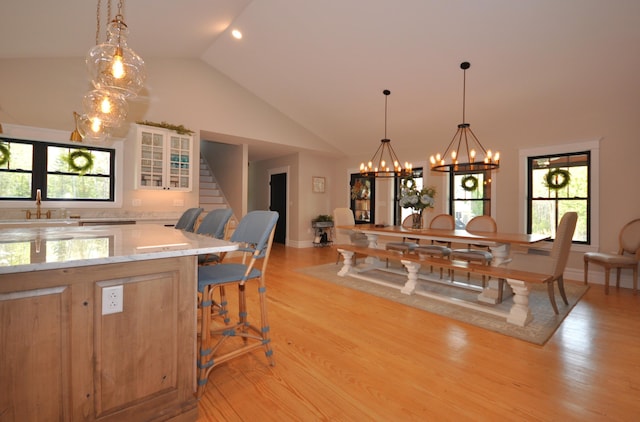 dining space featuring light hardwood / wood-style flooring, sink, high vaulted ceiling, and a chandelier