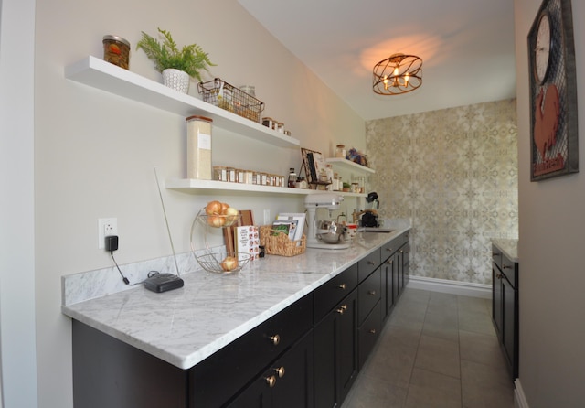 bar with dark tile patterned flooring, light stone counters, a notable chandelier, and sink