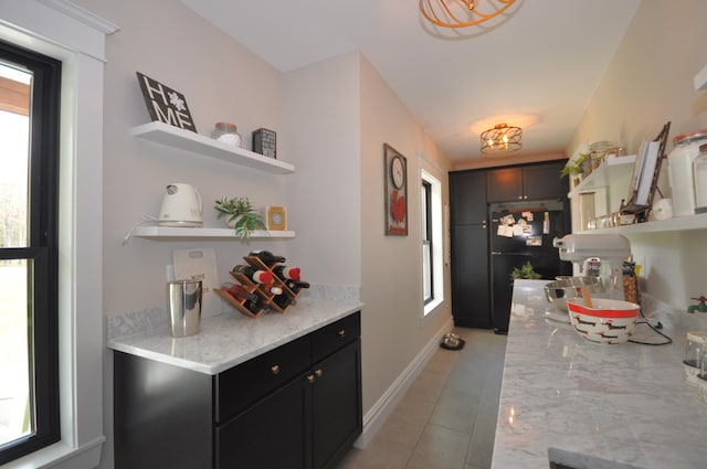 kitchen with black refrigerator, light stone countertops, plenty of natural light, and light tile patterned floors