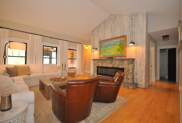 living room featuring a stone fireplace, vaulted ceiling, and hardwood / wood-style flooring