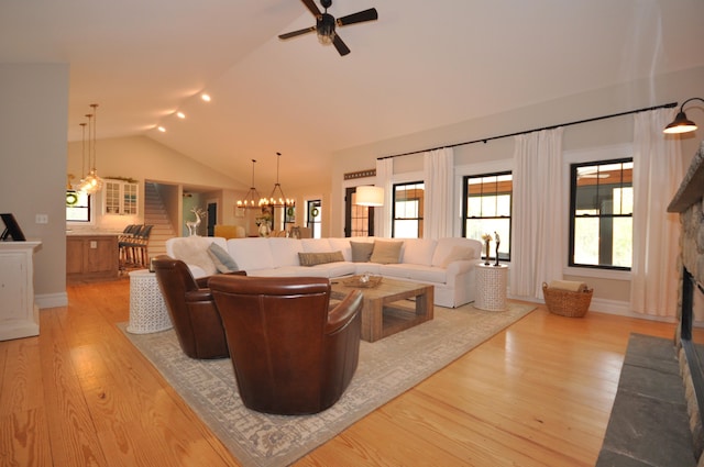 living room featuring ceiling fan with notable chandelier, light hardwood / wood-style floors, a stone fireplace, and lofted ceiling