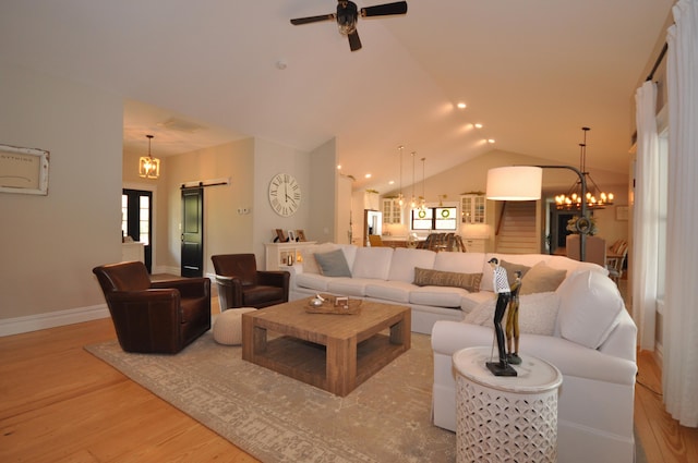 living room featuring a barn door, lofted ceiling, ceiling fan with notable chandelier, and light wood-type flooring