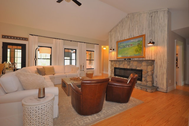 living room featuring lofted ceiling, ceiling fan, a stone fireplace, and light wood-type flooring