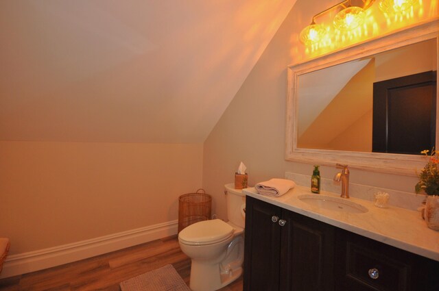 bathroom with wood-type flooring, vanity, toilet, and lofted ceiling