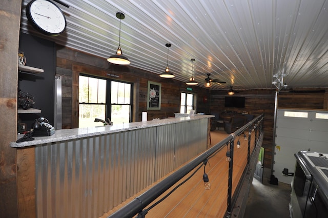 kitchen with wood walls, ceiling fan, light stone counters, and decorative light fixtures