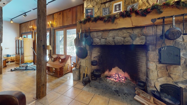 living room with rail lighting, wooden walls, a stone fireplace, and light tile patterned floors