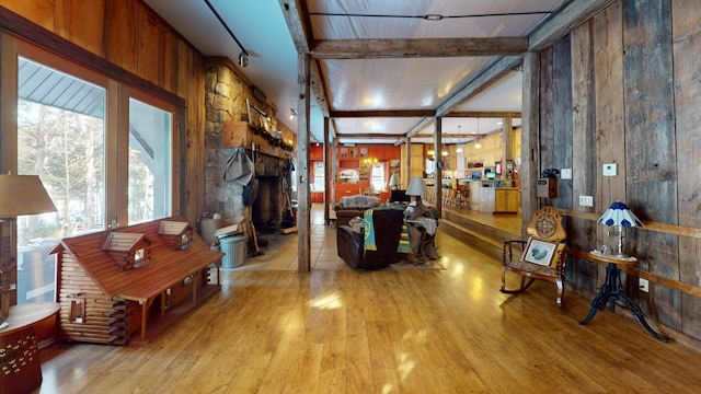 living room featuring beamed ceiling, wooden walls, a stone fireplace, and light wood-type flooring