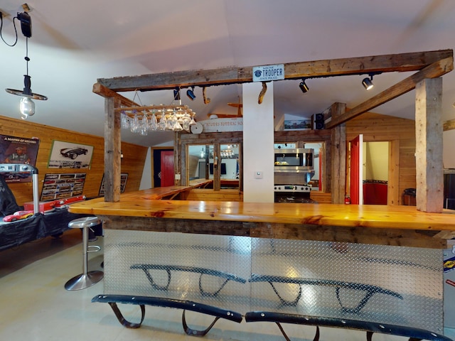 kitchen featuring concrete flooring, lofted ceiling with beams, appliances with stainless steel finishes, and wood walls