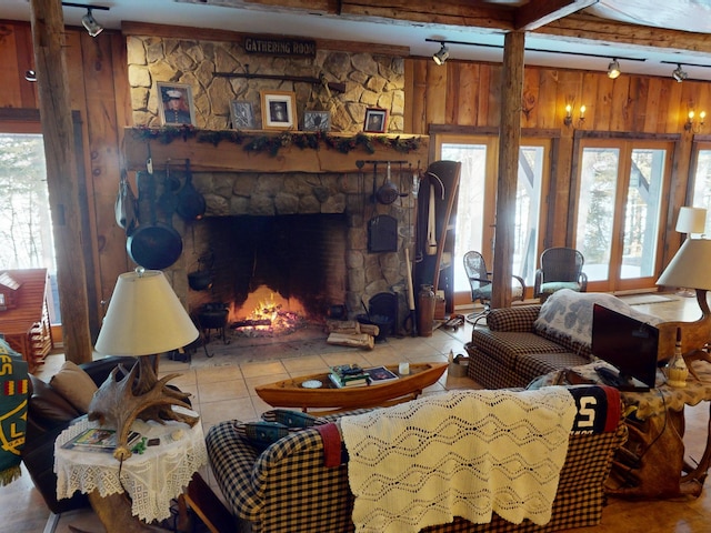 living room with tile patterned floors, a stone fireplace, track lighting, wooden walls, and beamed ceiling