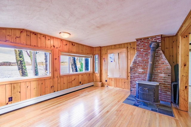 unfurnished living room featuring a textured ceiling, hardwood / wood-style flooring, a wood stove, and baseboard heating